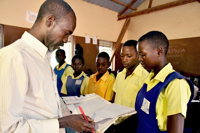 Teacher Adam Gabriel checks the work of his students Moses Justin, Daniel Adam and Salawa Emmanuel during a history lesson at St. Bakhita Primary School. Credit: GPE/Jok Solomon